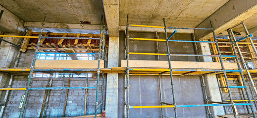A construction site with scaffolding and a wall in the background. The scaffolding is yellow and blue