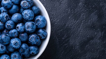  a close up of a bowl of blueberries on a black surface with drops of water on the top of the bowl. - obrazy, fototapety, plakaty
