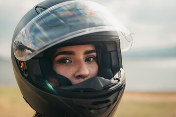 Close-up view of a woman's eyes as she looks out of a motorcycle helmet, with a serene lake and soft light in the background