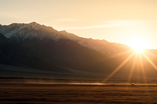Golden sunrise over snow-capped mountains with car traveling along the valley road