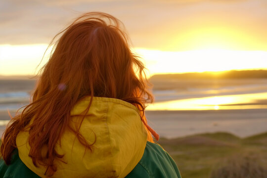 Young woman watching the sunset over a serene beach at dusk. View from the back