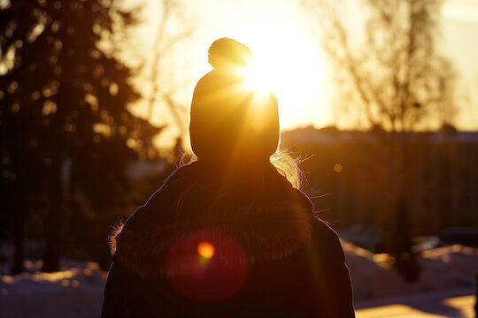 Winter sunset silhouette of a woman wearing a beanie against a golden sky. View from the back