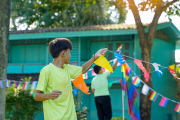 Two Asian boys decorate rainbow flags in front of their house and on trees around their house for...