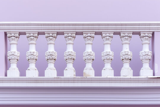 Close view of a Victorian millwork balcony with ornate balustrades against a pale violet background