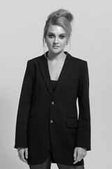 Beauty, fashion and make-up concept. Beautiful young blonde woman wearing black suit studio portrait. Girl with fancy hairstyle. Model standing still and looking at camera. Black and white image