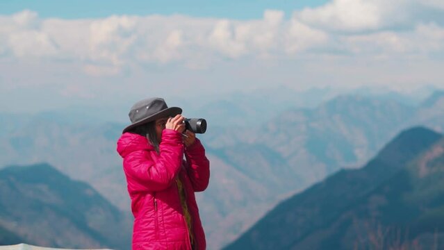 Hiker girl taking picture of mountains with camera at Jalori Pass, Himachal Pradesh, India. Summer vacation concept. Travel content creator taking photos for social media.