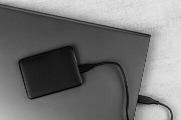 a closed laptop with a hard drive connected by a cable close-up on a gray background top view