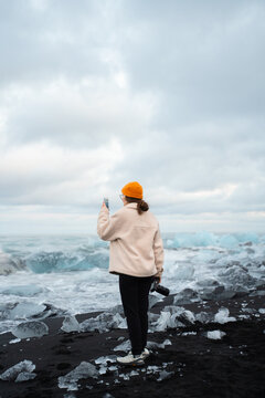 Woman takes picture of glacier with her phone camera at beach