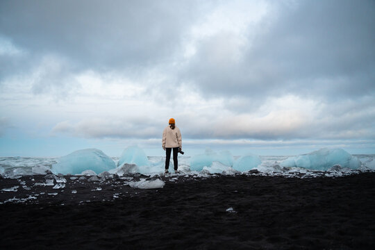 Woman with camera on ice floe, capturing beauty of massive glacier 