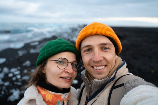 Joyful couple in love capturing selfie on black sand beach at ocean 