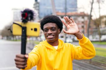 Young African influencer waves while streaming live on his mobile in a vibrant park.