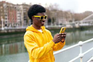 A cheerful african young man in yellow enjoys his phone outdoors.