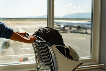 Close up of a passenger just before boarding taking a suitcase cart next to a window overlooking...