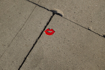 Red classic kiss lips-shaped piece of paper laying on a concrete floor