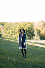 A young girl in a hat stands on the lawn in an autumn park