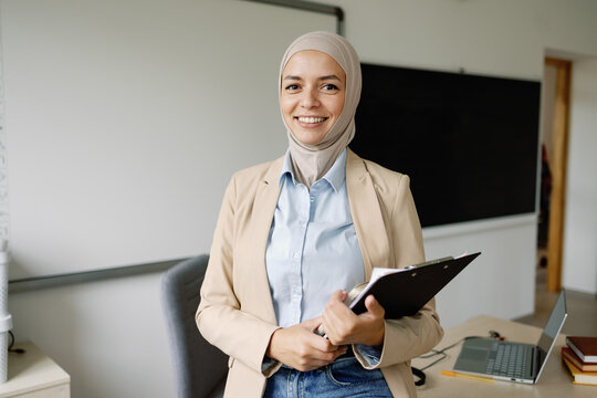 Cheerful teacher with clipboard in classroom