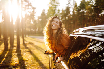 Young woman is resting and enjoying sunset in the car while traveling.  Lifestyle, travel, tourism,...