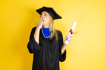 Beautiful blonde young woman wearing graduation cap and ceremony robe bored yawning tired covering...