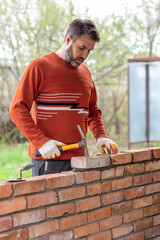a man builds a brick wall, puts a brick on a cement-sand mortar, tapping on the brick with a construction hammer