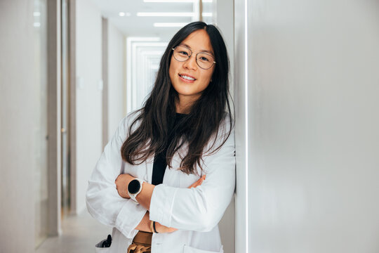 Smiling Asian woman doctor standing in hallway of clinic.