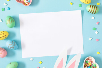 Easter party concept. Flat lay, top view of blank sheet of paper, easter bunny ears white pink blue...