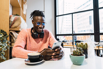 Cheerful black browsing smartphone in cafe