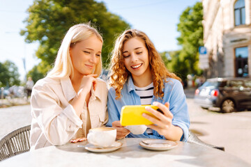 Two smiling woman are sitting in a cafe, drinking coffee, taking selfies, talking with friends....