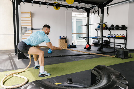 Man workout in the gym pulling weights with a rope
