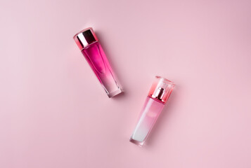 Two pink glass bottle with cosmetic product on a pastel pink background, top view