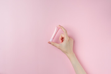 Woman's hands holding a small pink tube on pastel pink background
