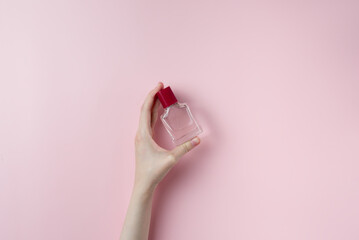Woman hands holding perfume on pastel pink background