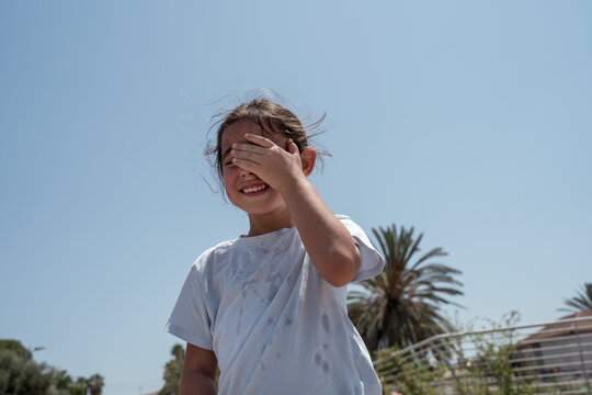 Little Brunette Girl Wiping Sweat with Hand on Hot Sunny Day.
