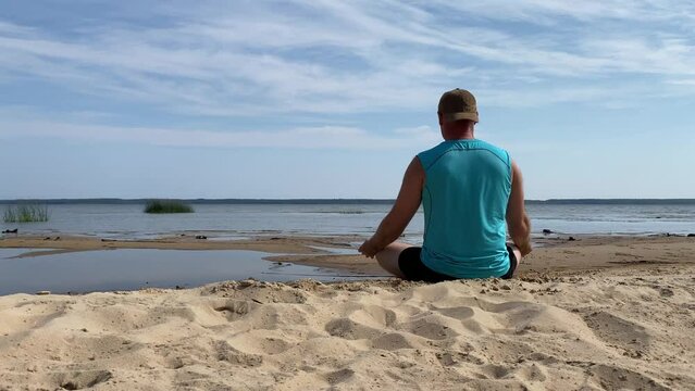 A man meditates on the shore of a lake in the lotus position in summer.