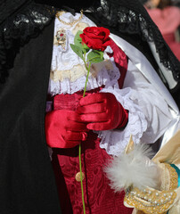 noble lover wearing red gloves hands a red rose to his beloved