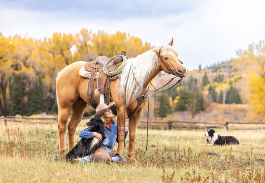 Colorado Cowgirl with a palomino horse and her herding dog in the mountains with colorful aspens in the background outtake