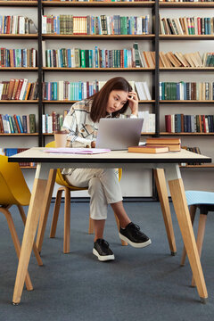 Confused Asian student doing homework in library