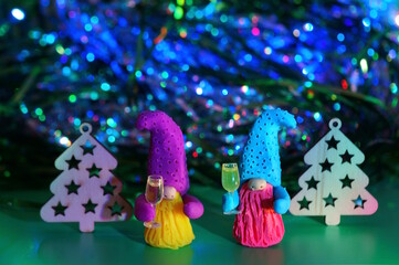 Two toy dwarfs made of plasticine with glasses of champagne on the background of Christmas decorations. New Year's holidays and Christmas. Decorations and decorations. Green background.