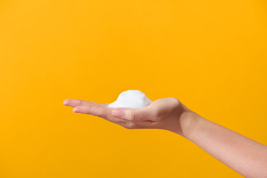 White soap bubbles in hand over yellow background