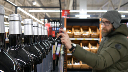 Close-up of many glass bottles of red wine in a wine shop and a male buyer takes one