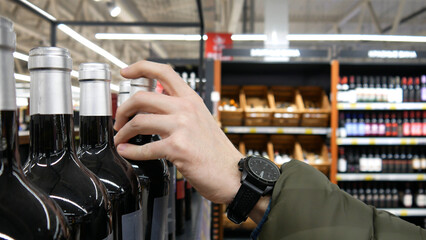 Close-up of a male buyer's hand taking a glass bottle of red wine in a wine shop