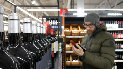 Close-up of many glass bottles of red wine and a male buyer chooses one - obrazy, fototapety, plakaty