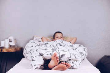 Bare feet. The boy is lying in bed covered with a blanket. Foot and heel. Flatfoot