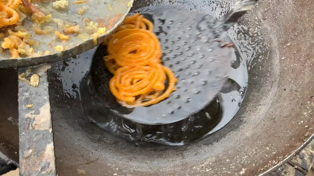 man making traditional sweet orange jalebi snacks on a street food market in Punjab Pakistan. Frying jalebi in big oil pan at street stall.
