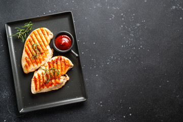 Grilled meat. Chicken steak with spices and ketchup. Top view on black table.
