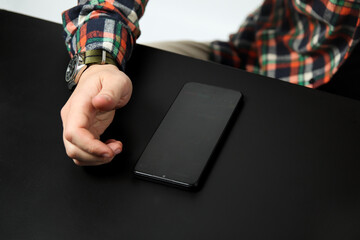 Black phone and male hand on the black table. Business concept. Top view. Close up