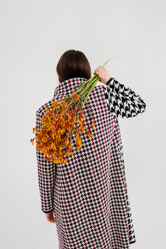 Unrecognizable woman in houndstooth trench coat with autumn flowers 