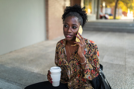 black woman having a coffee on the street while walking in the city