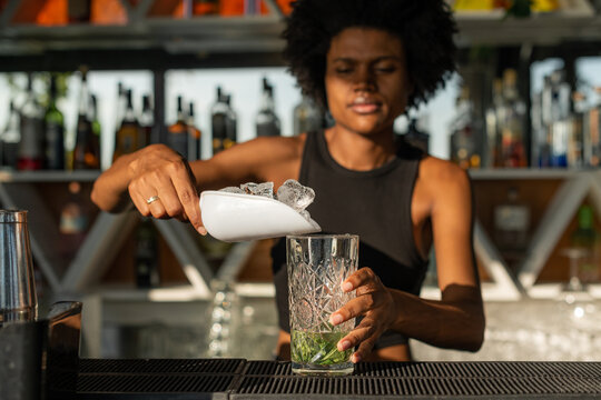 Black female bartender putting ice in a glass while preparing a 