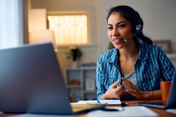 Hispanic woman talking during conference call while working remotely at home.