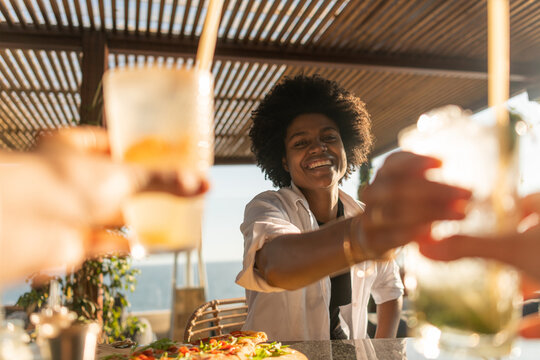 Female black client in a bar taking cocktail from anonymous bart